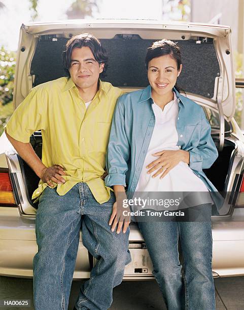 man and pregnant woman sitting on rear bumper of car, portrait - garcia stockfoto's en -beelden