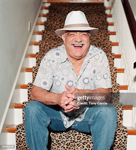 mature man wearing hat sitting at bottom of staircase, laughing - garcia stock-fotos und bilder