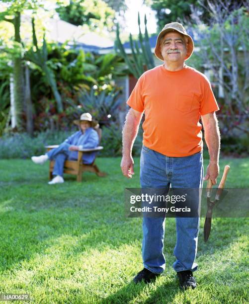 mature man outside holding plant clippers, wife in background - garcia stock-fotos und bilder