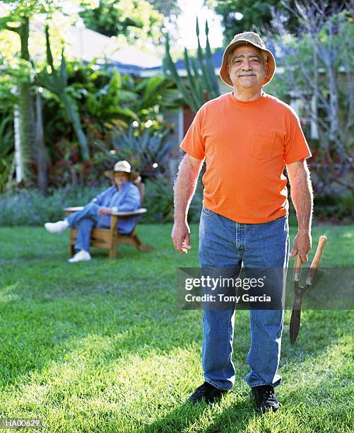 mature man outside holding plant clippers, wife in background - garcia stockfoto's en -beelden