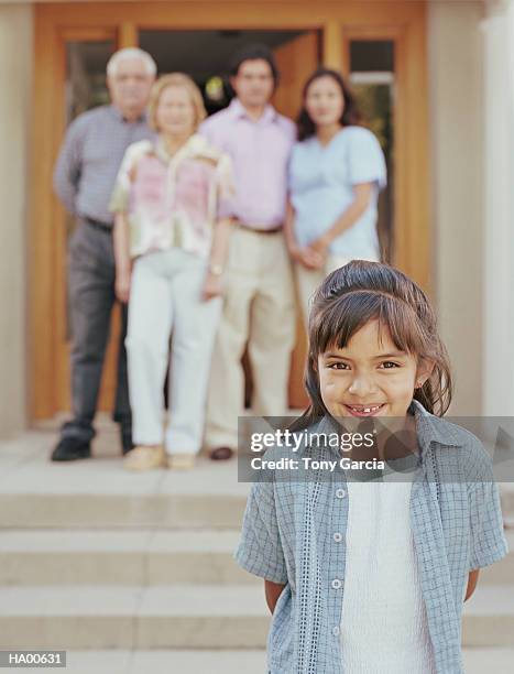 girl (4-6) in front of house, family in background - garcia stockfoto's en -beelden