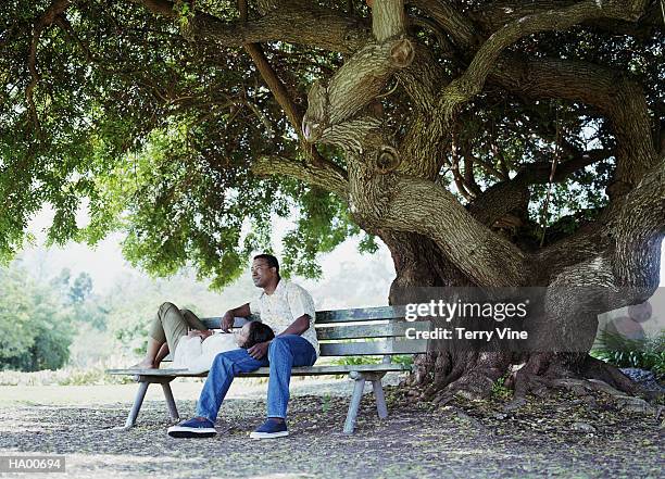 couple relaxing on bench, under brazilian pepper tree - brazilian pepper tree stock pictures, royalty-free photos & images