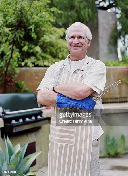 mature man wearing apron, standing next to barbeque, portrait - bbq apron stock pictures, royalty-free photos & images