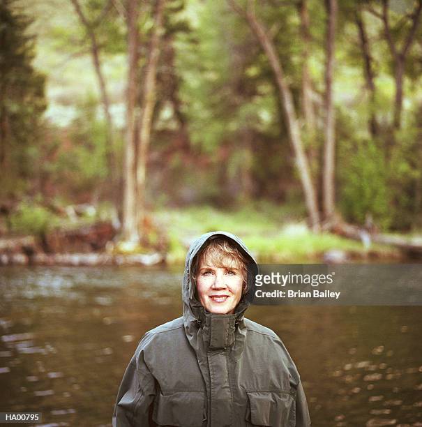mature woman wearing raincoat, standing in river - brian stock-fotos und bilder