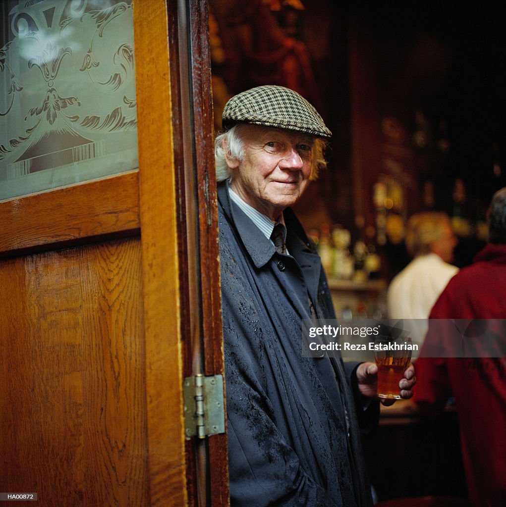 Mature man wearing hat, holding glass of beer, portrait