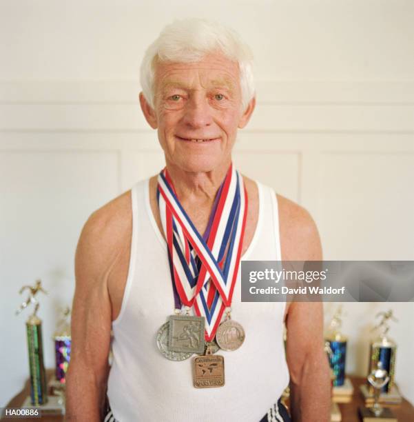 mature man wearing marathon medals, trophys in background - waldorf fotografías e imágenes de stock