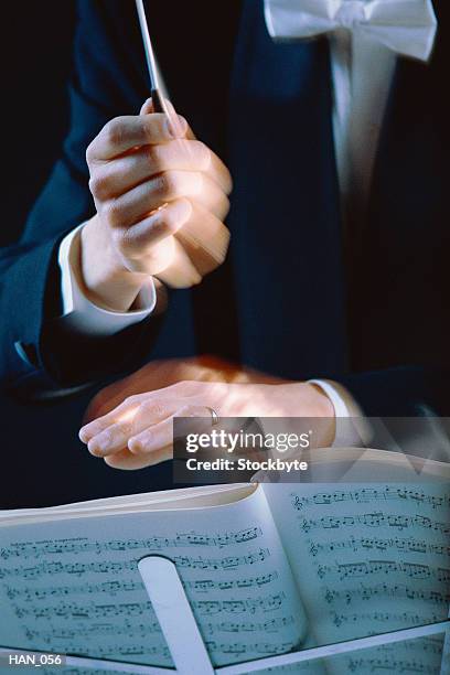 conductor's hands waving baton over music stand - classical orchestral music stock pictures, royalty-free photos & images