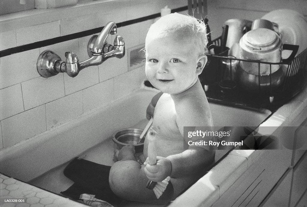 Baby (9-12 months) sitting in kitchen sink, portrait (B&W)