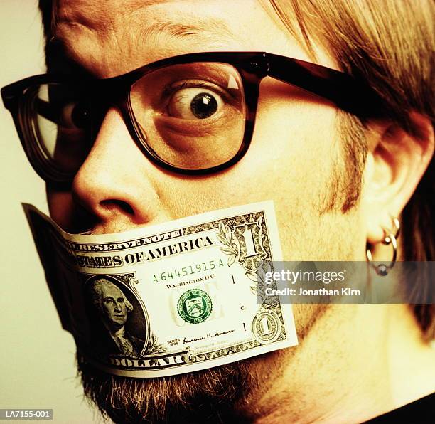young man with us one dollar bill covering mouth, close-up - money talks stock pictures, royalty-free photos & images