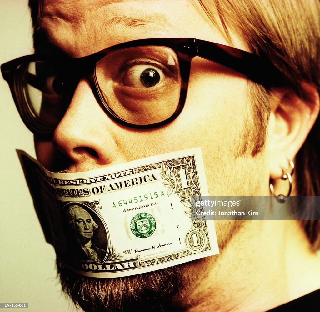 Young man with US one dollar bill covering mouth, close-up