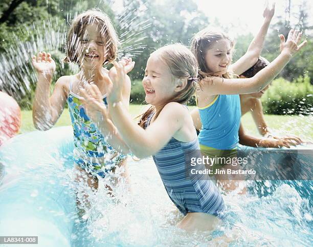 group of children (4-10) splashing in paddling pool in garden - planschbecken stock-fotos und bilder