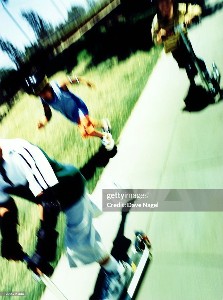 Three boys (5-9) on scooters and skates (blurred motion)