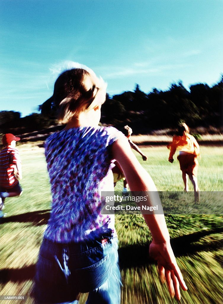 Group of children (5-10) running outdoors, rear view (blurred)