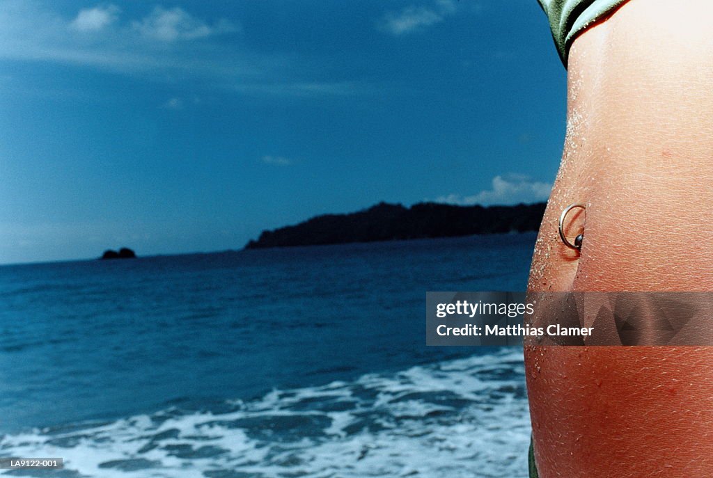 Woman on beach with belly ring, mid section, close-up