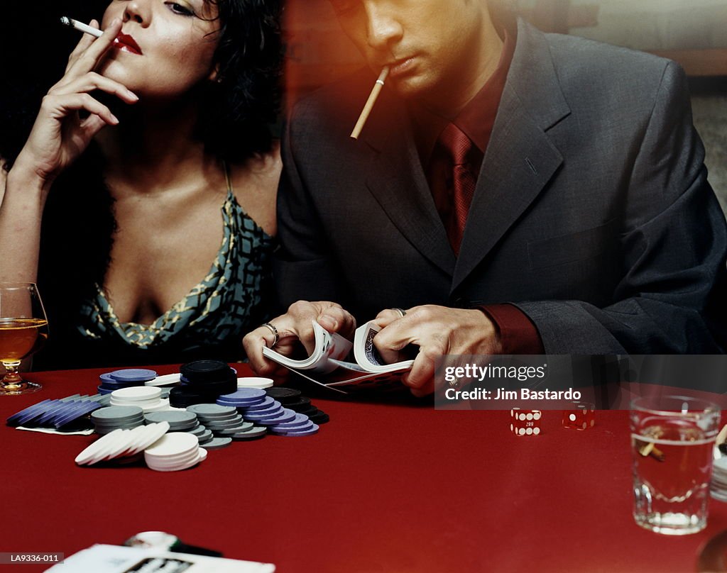 Man and woman at card table, man shuffling deck of cards