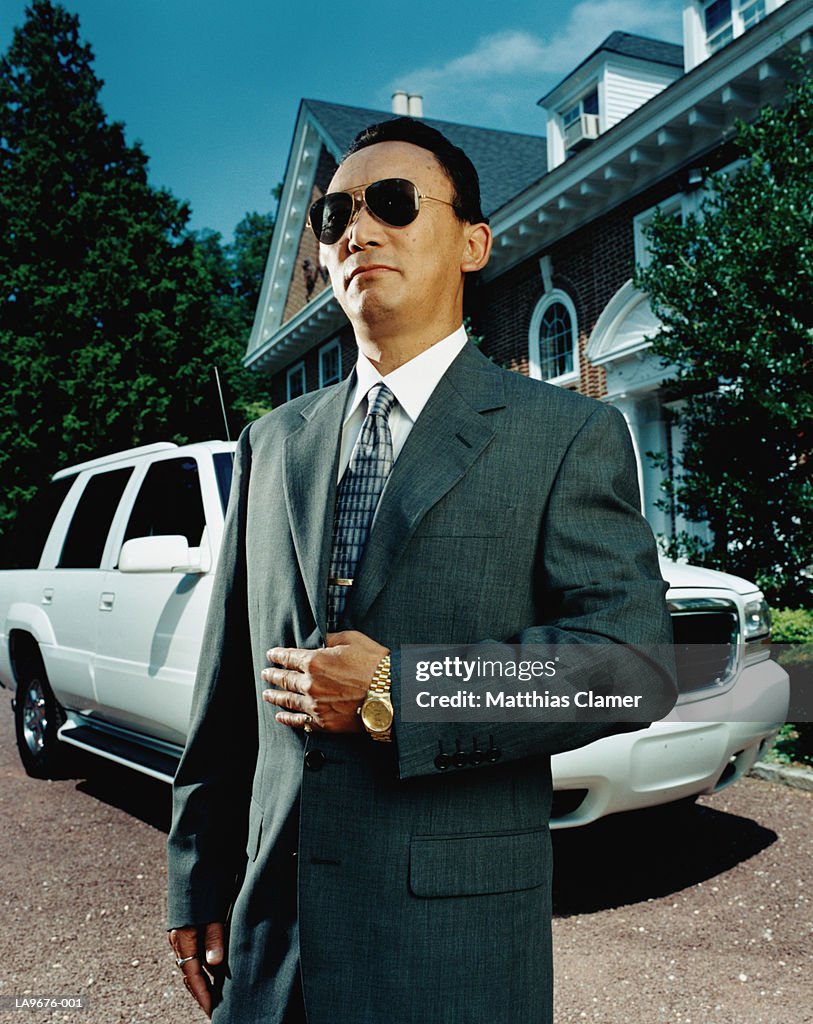 Suited man with car outside house, portrait