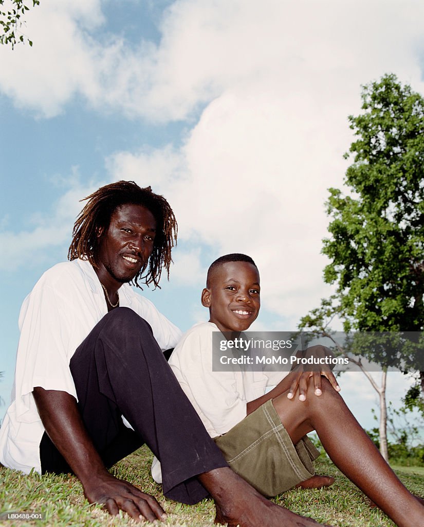 Father and son (9-11) sitting on grass, portrait