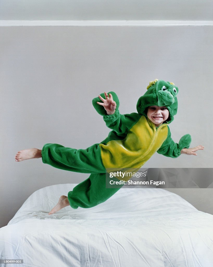 Boy (4-6) in monster costume jumping on bed