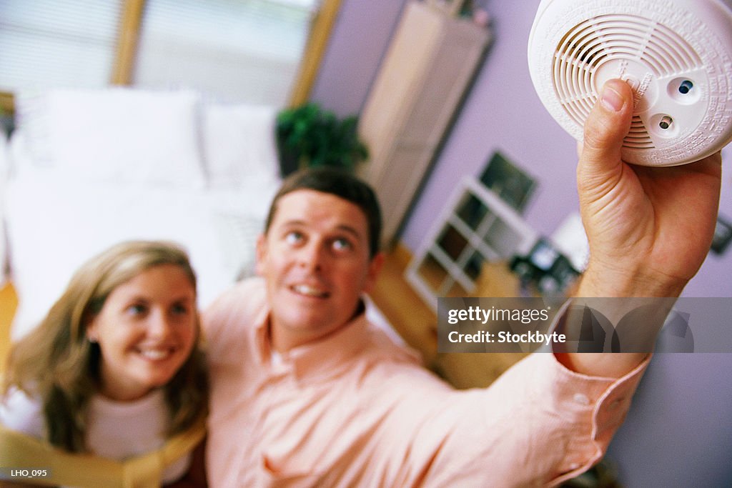 Woman looking as man installs smoke detector
