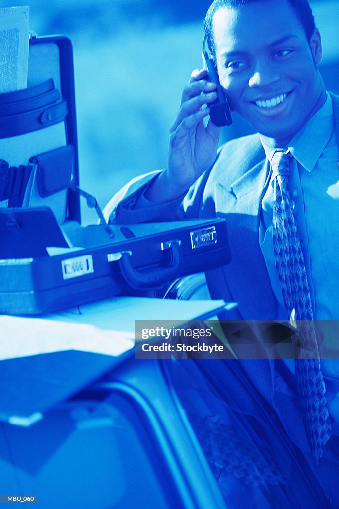 Man talking on cellular phone, briefcase on car roof