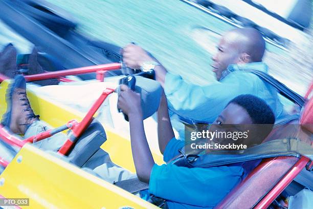 father and son driving go-carts, son looking towards camera - fahrspaß stock-fotos und bilder