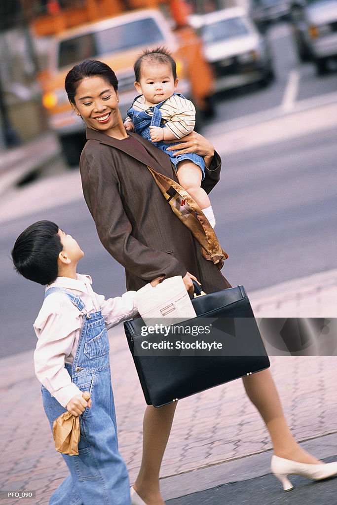 Mother carrying infant and holding son's hand while crossing street