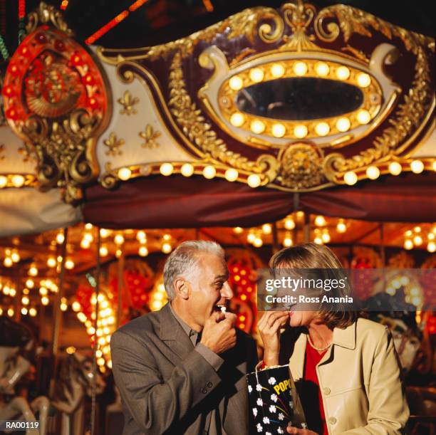 man and woman standing in front of carousel eating popcorn - ross stockfoto's en -beelden