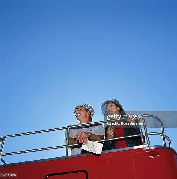 man and woman riding on top deck of double-decker bus, low angle view - double deck bus stock-fotos und bilder