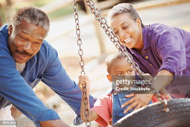 man and woman pushing boy sitting in tire swing - schaukel mann stock-fotos und bilder