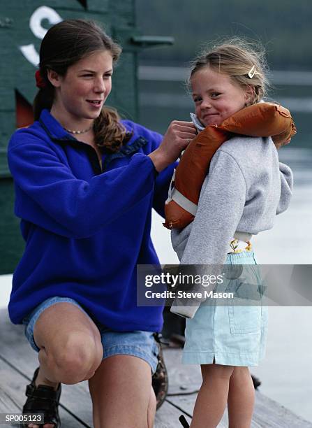 teen girl putting a life jacket on her sister - equipamento marítimo de segurança imagens e fotografias de stock