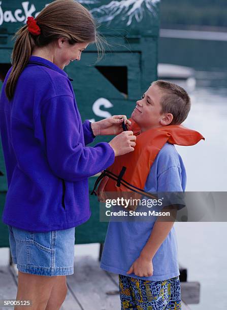 teen girl putting a life jacket on her brother - equipamento marítimo de segurança imagens e fotografias de stock