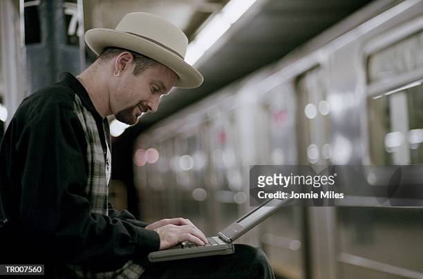 man using a laptop while waiting for the subway - only mid adult men foto e immagini stock