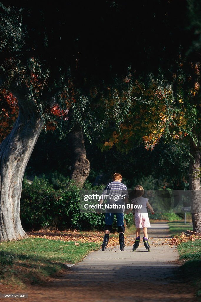 Two children (6-10) in-line skating along street, rear view