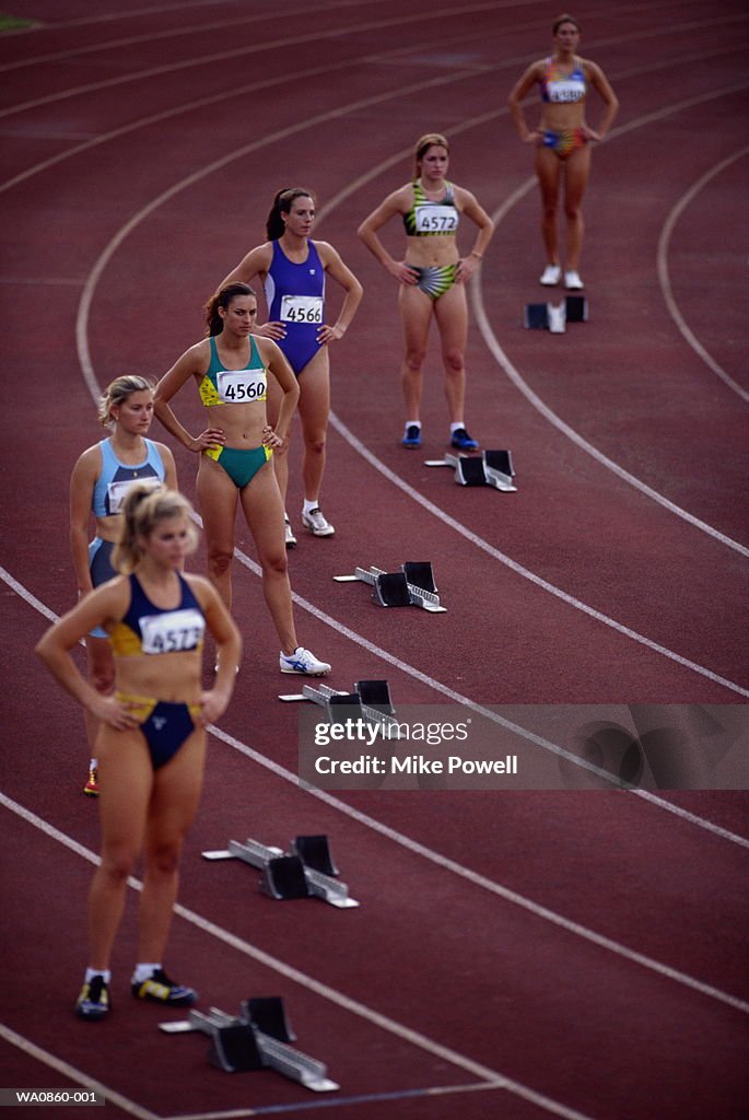 Female athletes standing behind starting blocks on track, elevated