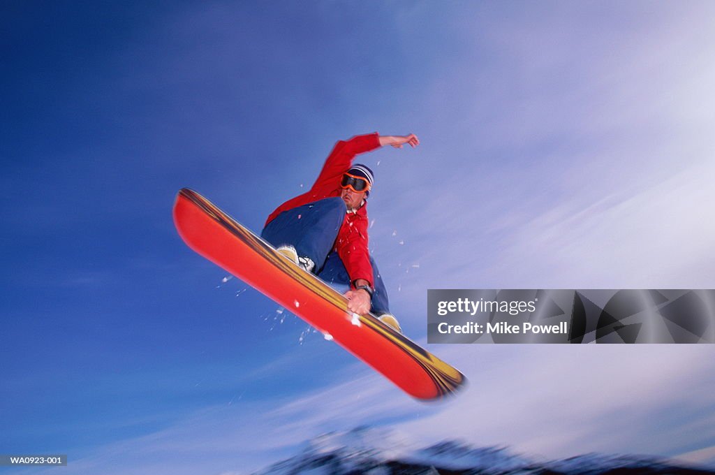 Male snowboarder in mid-air, low angle view (blurred motion)