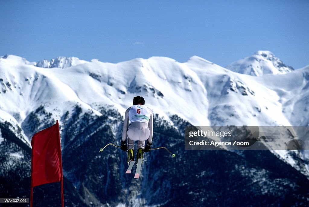 Downhill skier in mid-air jump, mountains in background, rear view
