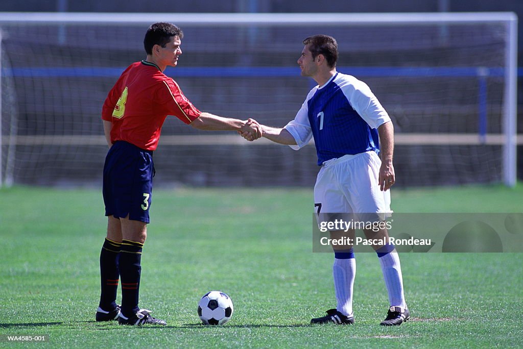 Two opposing soccer players shaking hands on field