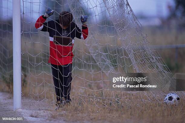 soccer goalkeeper (10-12) holding netting, ball in goal area - amateur stock-fotos und bilder