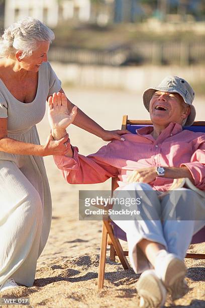 woman trying to pull man out of beach chair; man laughing - next to stock-fotos und bilder