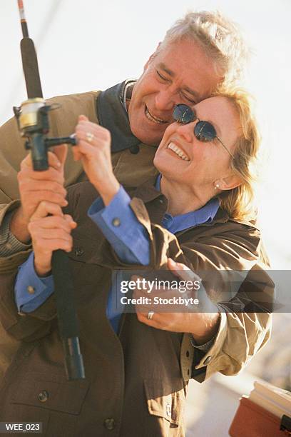 man standing behind woman, helping her hold fishing pole - her stock pictures, royalty-free photos & images