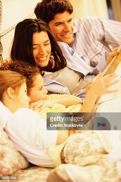 parents and two children lying in bed and reading - bedtime stories stock-fotos und bilder