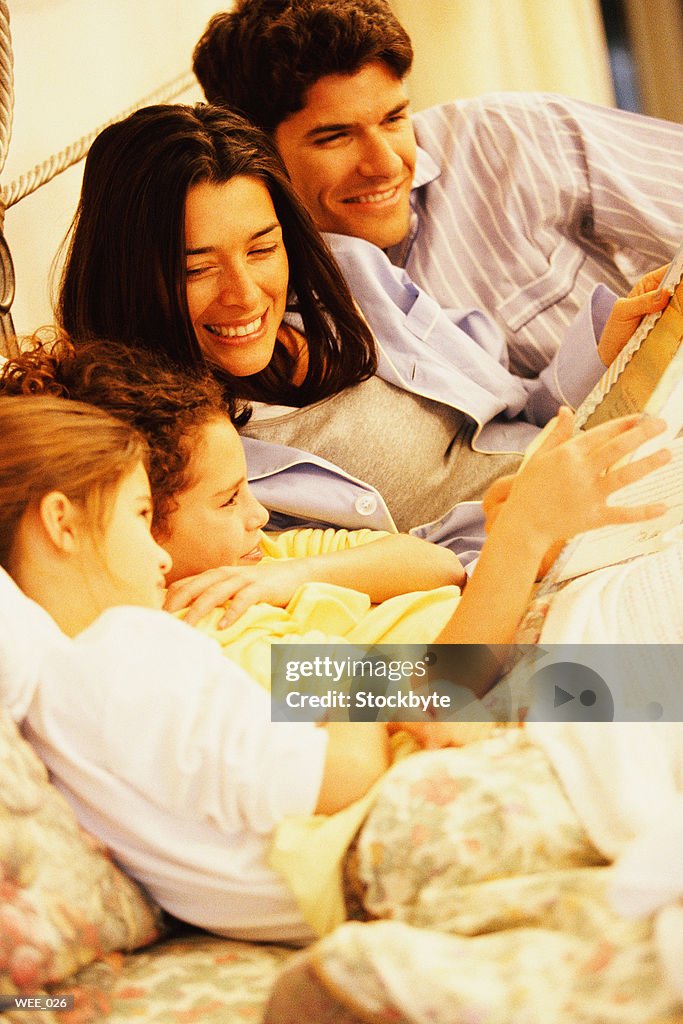 Parents and two children lying in bed and reading