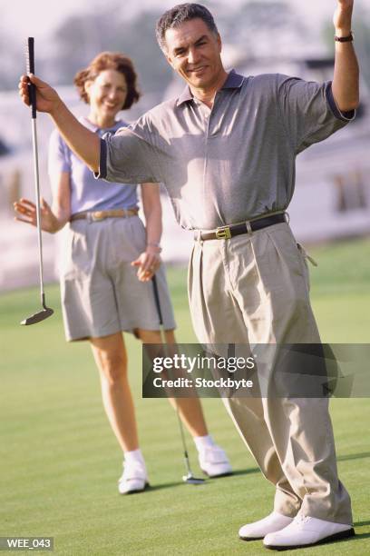 man on golf course raising his arms; woman in background - menschliche gliedmaßen stock-fotos und bilder