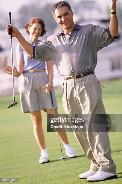 man on golf course raising his arms; woman in background - human limb stock pictures, royalty-free photos & images