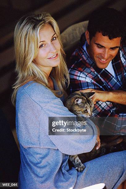 woman cuddling cat; man beside her petting it - her stock pictures, royalty-free photos & images