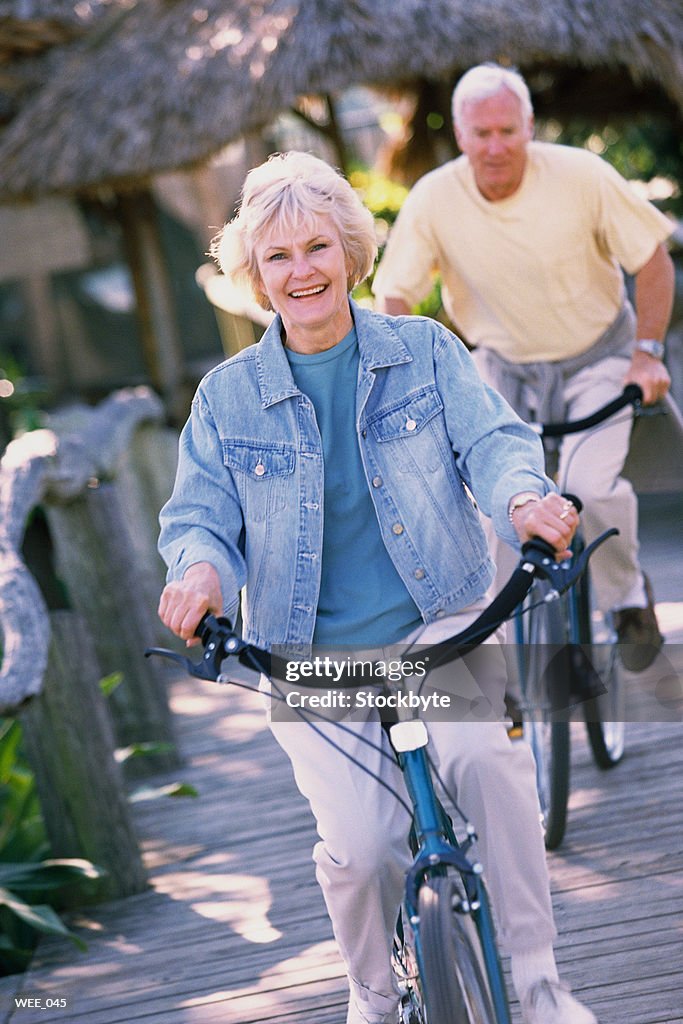 Woman and man riding bicycles along wooden sidewalk