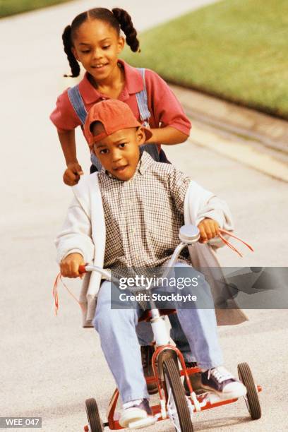 boy riding tricycle; girl running behind him - human powered vehicle stock pictures, royalty-free photos & images