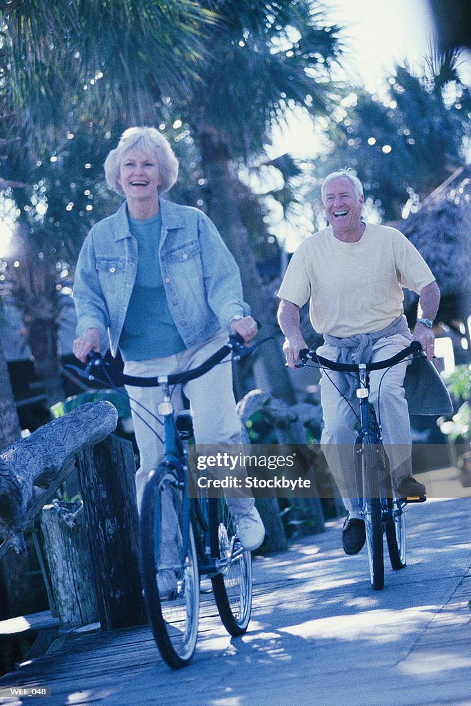 Woman and man riding bicycles along wooden sidewalk