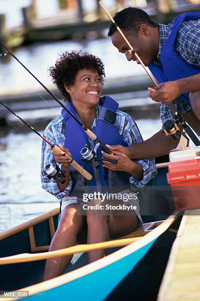 man on dock passing fishing gear to woman in canoe - next to stock pictures, royalty-free photos & images