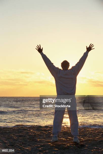 man standing on beach at sunset, arms raised in air - miembro humano fotografías e imágenes de stock